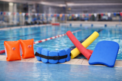 Schwimmhilfen im Vergleich am Beckenrand: Schwimmflügel, Schwimmgürtel, Schwimmnudel und Schwimmbrett in einem Hallenbad